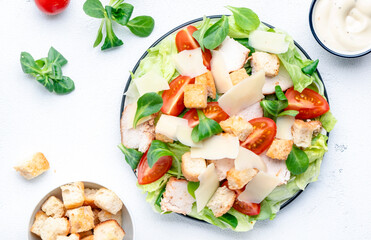 Caesar salad with chicken, iceberg salad, croutons, parmesan cheese and tomatoes with caesar dressing. White table background, top view - obrazy, fototapety, plakaty