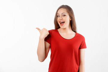 Surprised lovely girl points left at promo banner, shows advertisement on blank white space. Young brunette female looking amazed by promotion offer, stands over white background