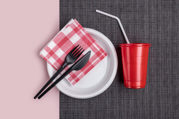 Plastic disposable tableware, cutlery on a dark napkin. Pink background, vertical studio shot.