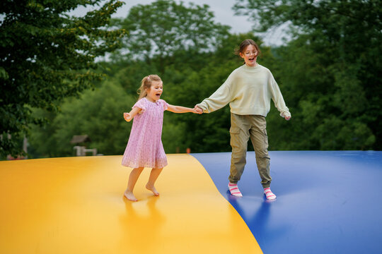 Little preschool girl and school sister jumping on trampoline. Happy funny children, siblings in love having fun with outdoor activity in summer. Trampolin in ukrainian flagg colors