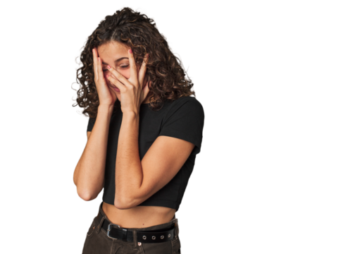 Radiant young woman with stunning curls blink through fingers frightened and nervous.