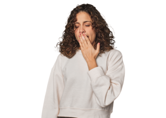 Radiant young woman with stunning curls yawning showing a tired gesture covering mouth with hand.
