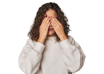 Radiant young woman with stunning curls afraid covering eyes with hands.