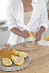 Fototapeta na wymiar Preparation of fresh llemonade. Young girl squeezes lemon juice in the kitchen near the window