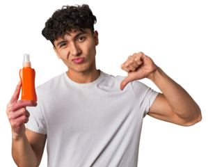 A young latin man holding a solar protection cream showing a dislike gesture, thumbs down. Disagreement concept.