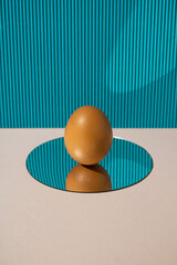 Fresh chicken egg reflecting in mirror on blue and beige background. Minimal concept.