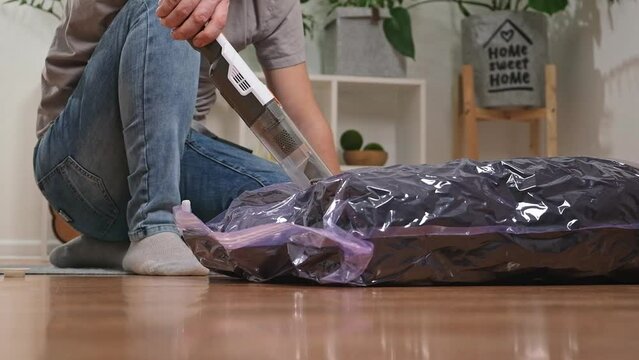 A man removes air from a vacuum bag using a manual vacuum cleaner. Winter jackets in a vacuum bag for seasonal storage in closet. Space saving and careful storage of clothes. Organization of storage.