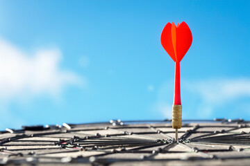 Dart in bullseye of dartboard target with blue sky background hitting target, goal and success