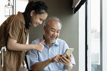 Teenager niece teaching showing thumb up to her happy smiling grandfather with smartphone, concept...
