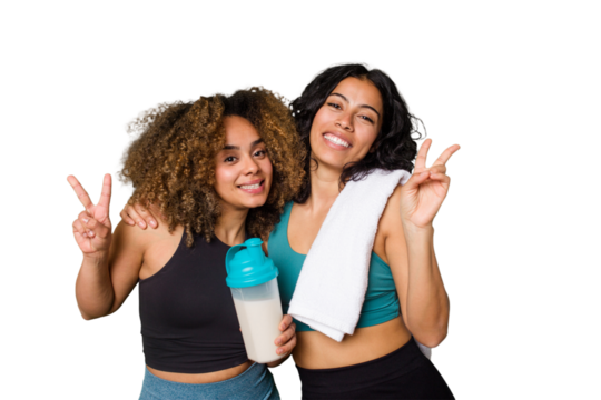 Two best friends are ready to go to the gym, one of them holds a protein shake, joyful and carefree showing a peace symbol with fingers.