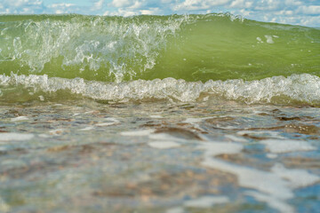 Small waves calmly run onto the pebbly shore. Background with an empty seashore on a warm summer day.