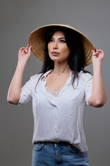 a beautiful brunette woman with a Vietnamese hat posing in the studio.
