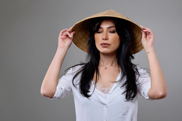 a beautiful brunette woman with a Vietnamese hat posing in the studio.