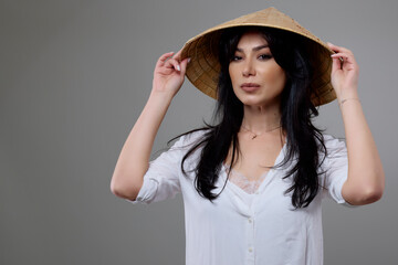 a beautiful brunette woman with a Vietnamese hat posing in the studio.