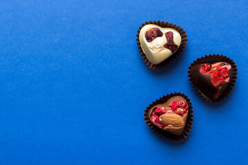 chocolate sweets in the form of a heart with fruits and nuts on a colored background. top view with space for text, holiday concept