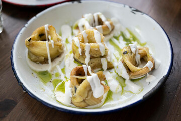 Smoked eggplant rolls on top of mozzarella cheese slices, in yogurt sauce, olive oil and pesto