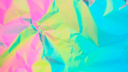 The surface of the crumpled foil is highlighted in different colors. Background holographic iridescent multicolored texture.