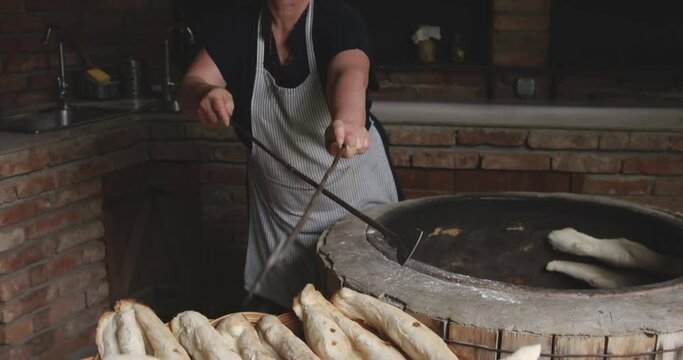 Woman Baker Removing The Baked Shoti Bread From A Rustic Round Clay Oven Using An Iron Stick.  Sighnaghi, Kakheti, Georgia - Slow Motion