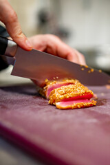 chef hands cut tuna into slices on a board in a restaurant kitchen