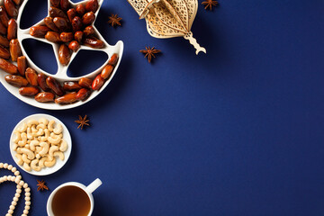 Ramadan Kareem Muslim food. Trays of dates and nuts, wooden lantern in form of mosque on dark blue...