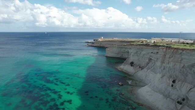 Malta's Ras il- Fenek Limestone Cliff Side, With Tropical Turquoise Water, Blue Sky And Fluffy White Clouds
