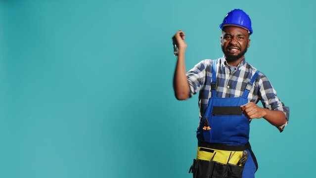 Construction worker hitting something with hammer, using manual metallic tool for renovation and building job. Young builder in uniform and hardhat holding mullet instrument on camera.