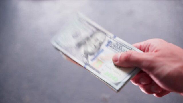 A hand holds out a stack of hundred dollar bills. Cash settlement process close-up