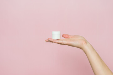 White jar or tube with cream (ointment) in hand. Facial care, bottle with cosmetic product without labeling.