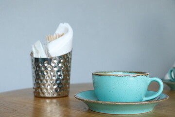 Iron cup for sugar sachets, napkins and coffee sticks on a wooden table. Сup of coffee. Gray wall