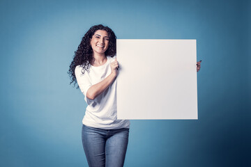 Obraz na płótnie Canvas Beautiful curly woman holding blank billboard isolated on blue background
