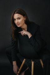 Portrait of a modern stylish woman. Beautiful brunette woman posing on a chair on a black background.