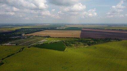 Green and yellow agricultural farm fields, fast moving shadows on the earth from white clouds in sky on a summer day. Agricultural panoramic landscape. Agrarian plantations scene. Aerial drone view.