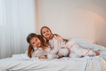 Fototapeta na wymiar Cheerful and positive two little girls are playing and having fun together in bedroom