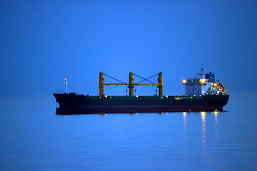 Glowing ship in the evening on the sea horizon with highlights on the water under the blue sky and...