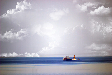 Tugboat, cranes and a ship on the sea horizon under a cloudy sky
