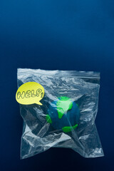 Earth Day. Globe enclosed in plastic bag with HELP message on blue background.