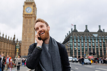 Happy bearded man talking on the phone while standing on the background of the Big Ben tower