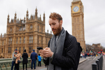 Portrait of a focused man with a smartphone in his hands against the backdrop of the London Big Ben...