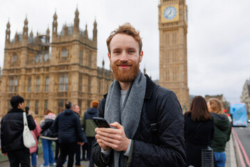 Portrait of a happy man with a smartphone in his hands standing on the Westminster Bridge against...