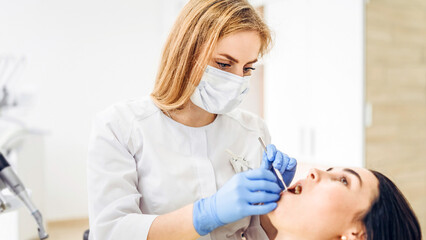 Female dentist with female patient in dental chair providing oral cavity treatment.