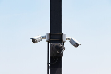 High angle photo circuit surveillance camera (CCTV) attached color black steel pole. Blue sky with bright sunlight as background. Cameras can record events such as traffic, accidents prevent theft.