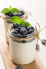 Two portion homemade Greek yogurt in a glass jars on white wood table. Healthy breakfast. Vertical orientation.