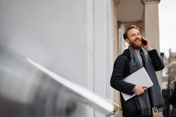 Laughing business man with laptop talking on the phone outdoor