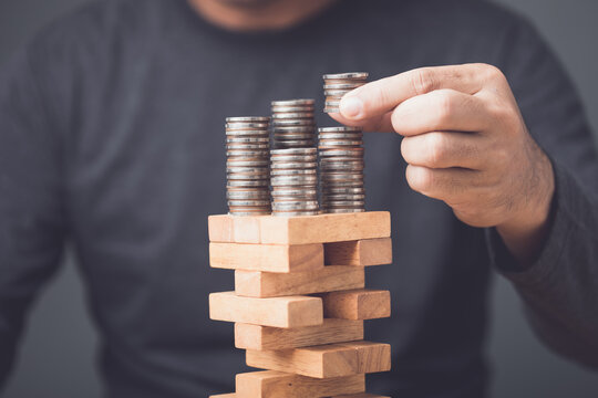 Investment contains certain risk. Idea of business man saving money, adding or removing coin on the top of risky situation tower wooden block game. Risks in business or financial concept.