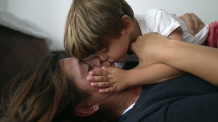 Mother and child love and affection. Little boy kissing mom on the lips. Family care and tenderness. Kid and mom together lying on couch