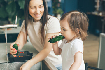 Mother and two-year-old daughter wash vegetables in the kitchen sink. Cooking and health care. Side view. Close-up.