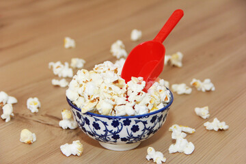 Fried white airy popcorn in a decorative plate and in a red spoon on a brown wooden background