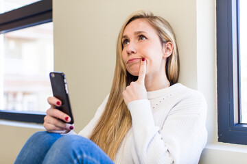 young adult pretty blonde woman using her smartphone at home