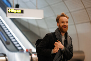 Portrait of happy male tourist with backpack on background of escalators at train station or airport