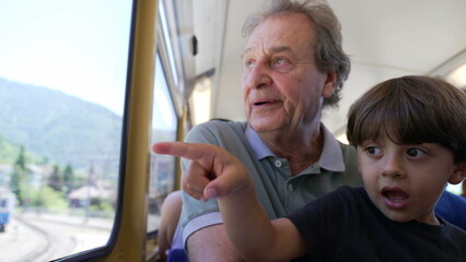 Grandfather traveling by train with grandchild seated by window looking at scenery. Senior man bonding with baby child together. Generational concept